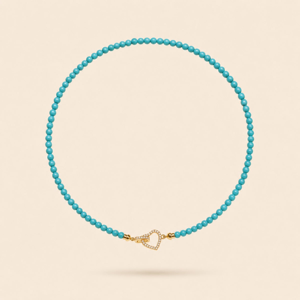 Little Crush natural turquoise bead necklace with a sparkling gold-tone heart clasp on an ivory background.